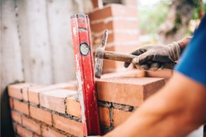 Brick Masonry performed by worker with a hammer and a leveler